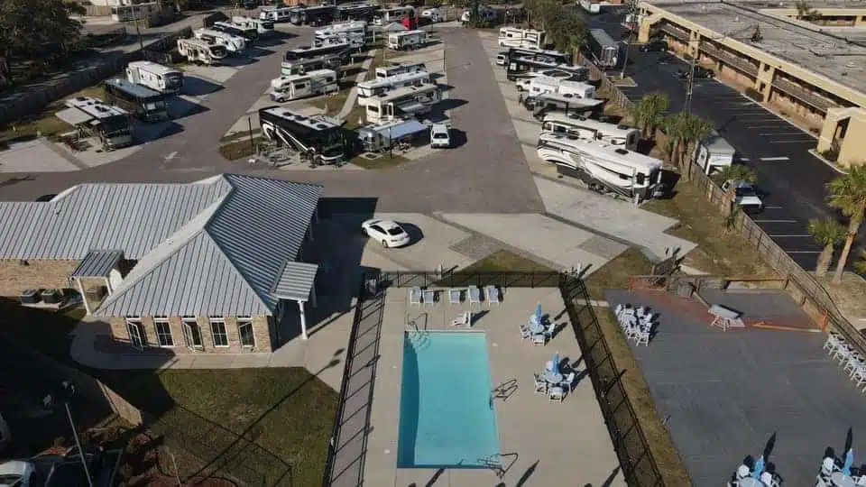 Aerial view of an RV park with multiple RVs, a building with a metal roof, a rectangular outdoor pool, and outdoor seating areas.