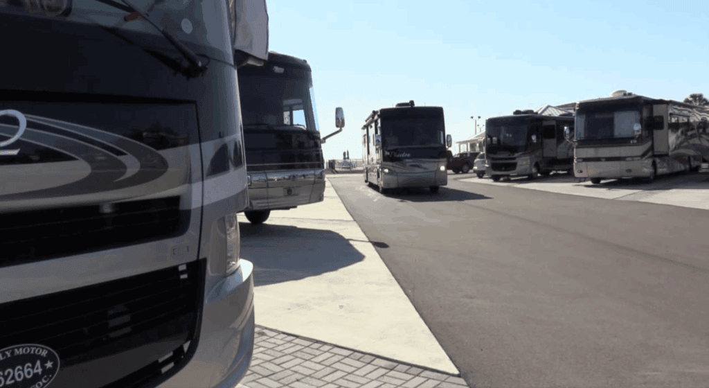 Several large recreational vehicles (RVs) are parked in designated spaces along a paved lot under a clear sky.