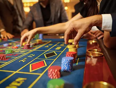 People place poker chips on a casino table during a game, with hands reaching in and chips stacked in different colors.