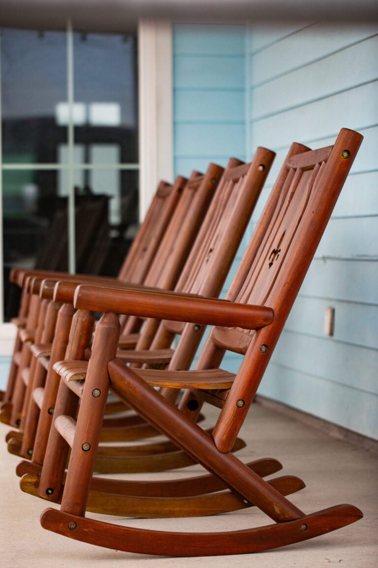 A row of wooden rocking chairs on a porch against a light blue wall.