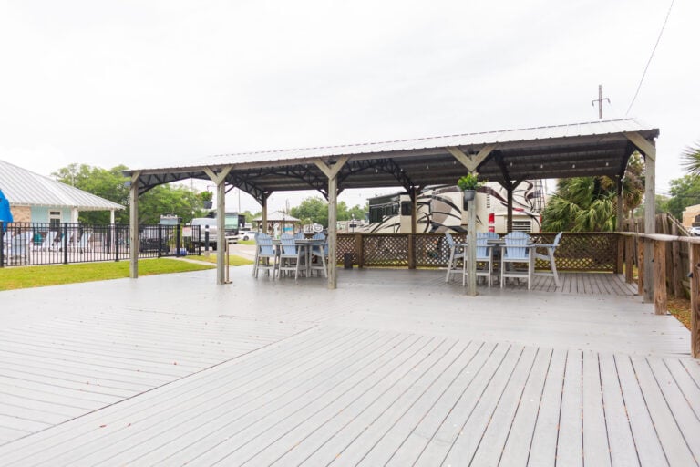A large outdoor pavilion with gray composite decking, featuring two sets of dining tables and chairs under a metal roof.