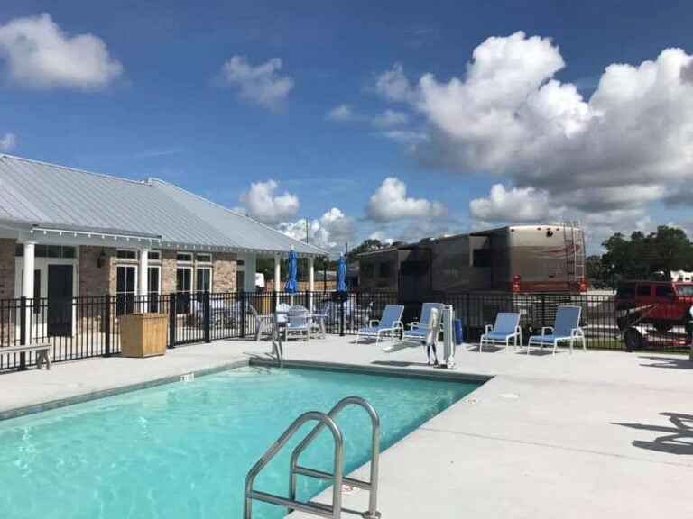 Swimming pool with lounge chairs and a metal fence, next to a building and a parked RV.