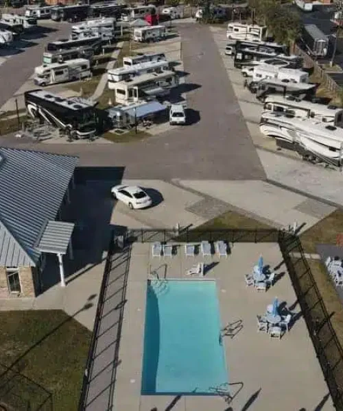 Aerial view of an RV park with multiple RVs, a building with a metal roof, a rectangular outdoor pool, and outdoor seating areas.