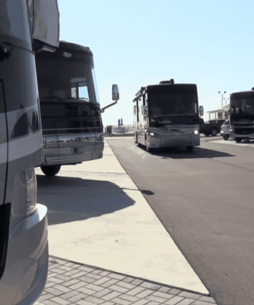 Several large recreational vehicles (RVs) are parked in designated spaces along a paved lot under a clear sky.
